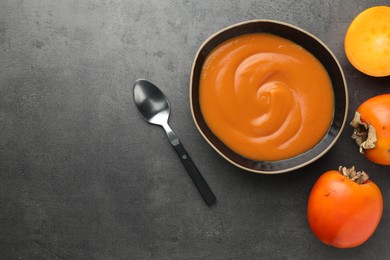 Delicious persimmon jam in bowl served on gray table, flat lay. Space for text