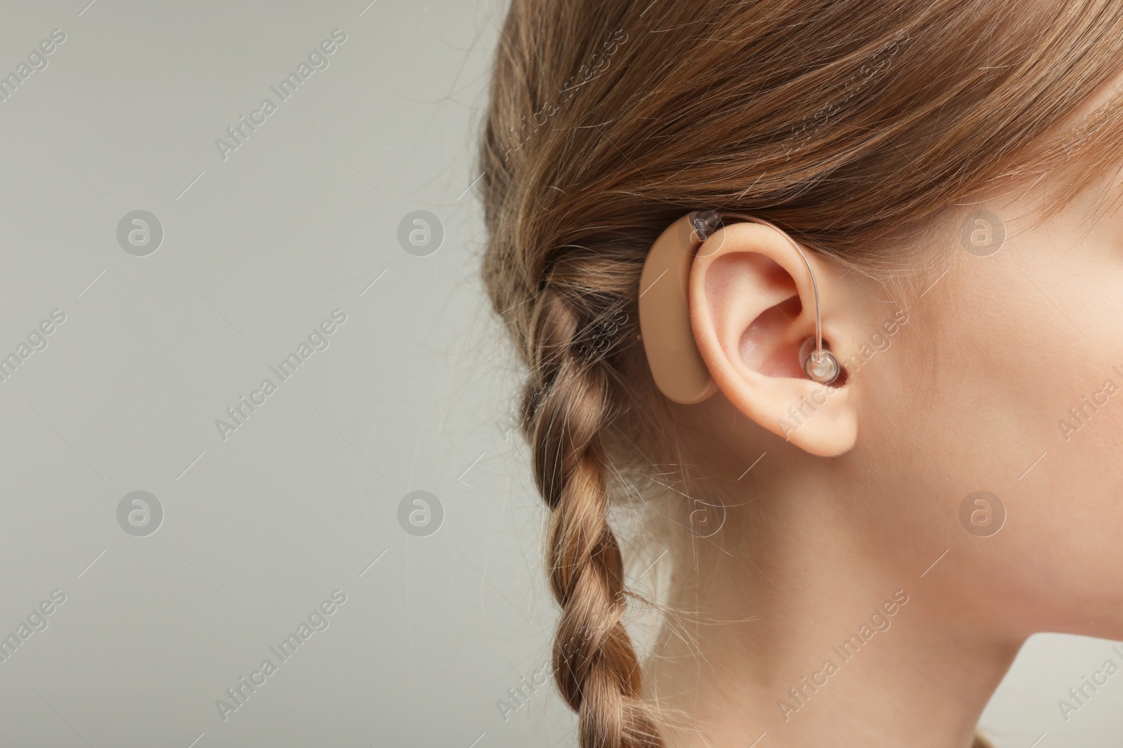 Photo of Little girl with hearing aid on grey background, closeup. Space for text