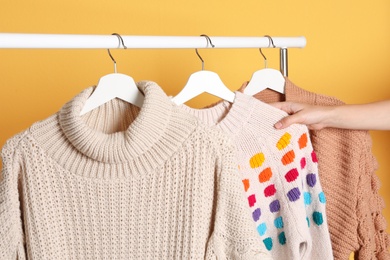 Woman choosing sweater on rack against color background