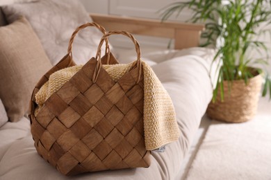 Stylish wicker basket with knitted blanket on sofa in living room, space for text