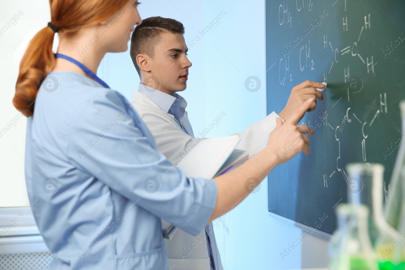 Photo of Scientists writing chemical formulas on chalkboard indoors