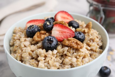 Photo of Tasty oatmeal with strawberries, blueberries and walnuts in bowl on white table, closeup