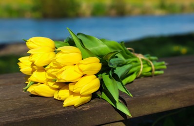 Bouquet of beautiful yellow tulips on wooden bench outdoors