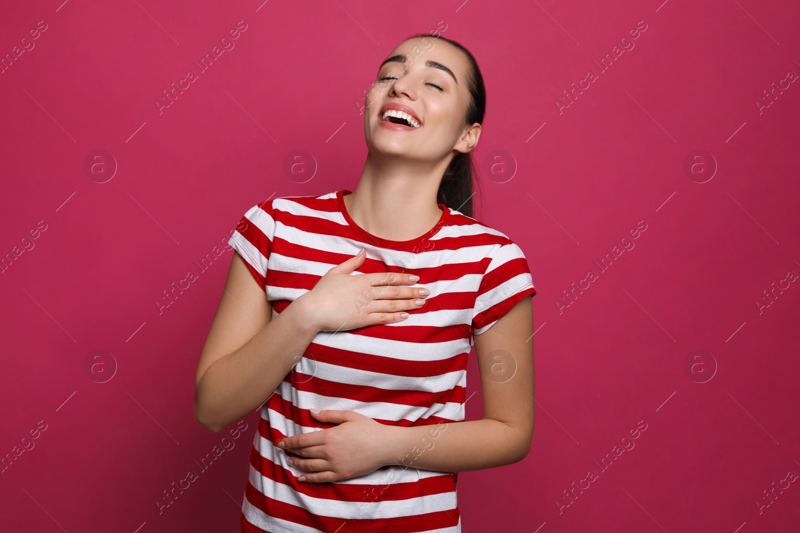 Photo of Beautiful young woman laughing on maroon background. Funny joke