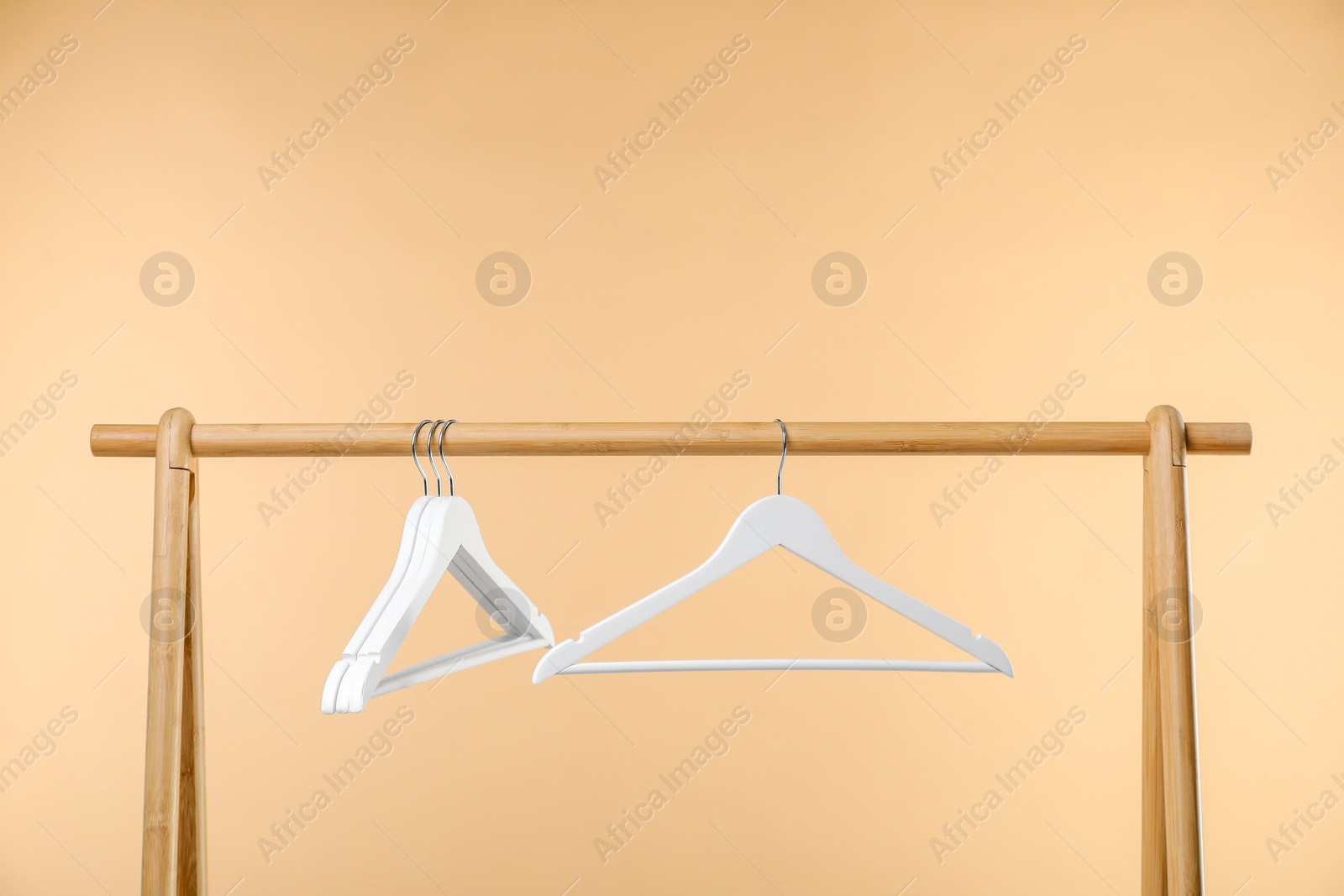 Photo of Empty clothes hangers on wooden rack against beige background