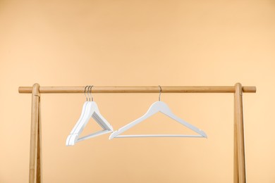 Photo of Empty clothes hangers on wooden rack against beige background