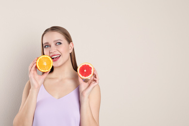 Young woman with cut orange and grapefruit on beige background, space for text. Vitamin rich food