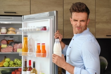 Man taking bottle with old milk out of refrigerator in kitchen