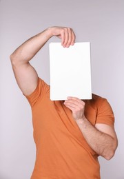 Man covering face with sheet of paper on light grey background. Mockup for design