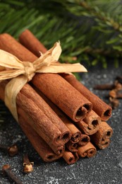 Photo of Different spices. Aromatic cinnamon sticks, clove seeds and fir branches on dark gray textured table, closeup