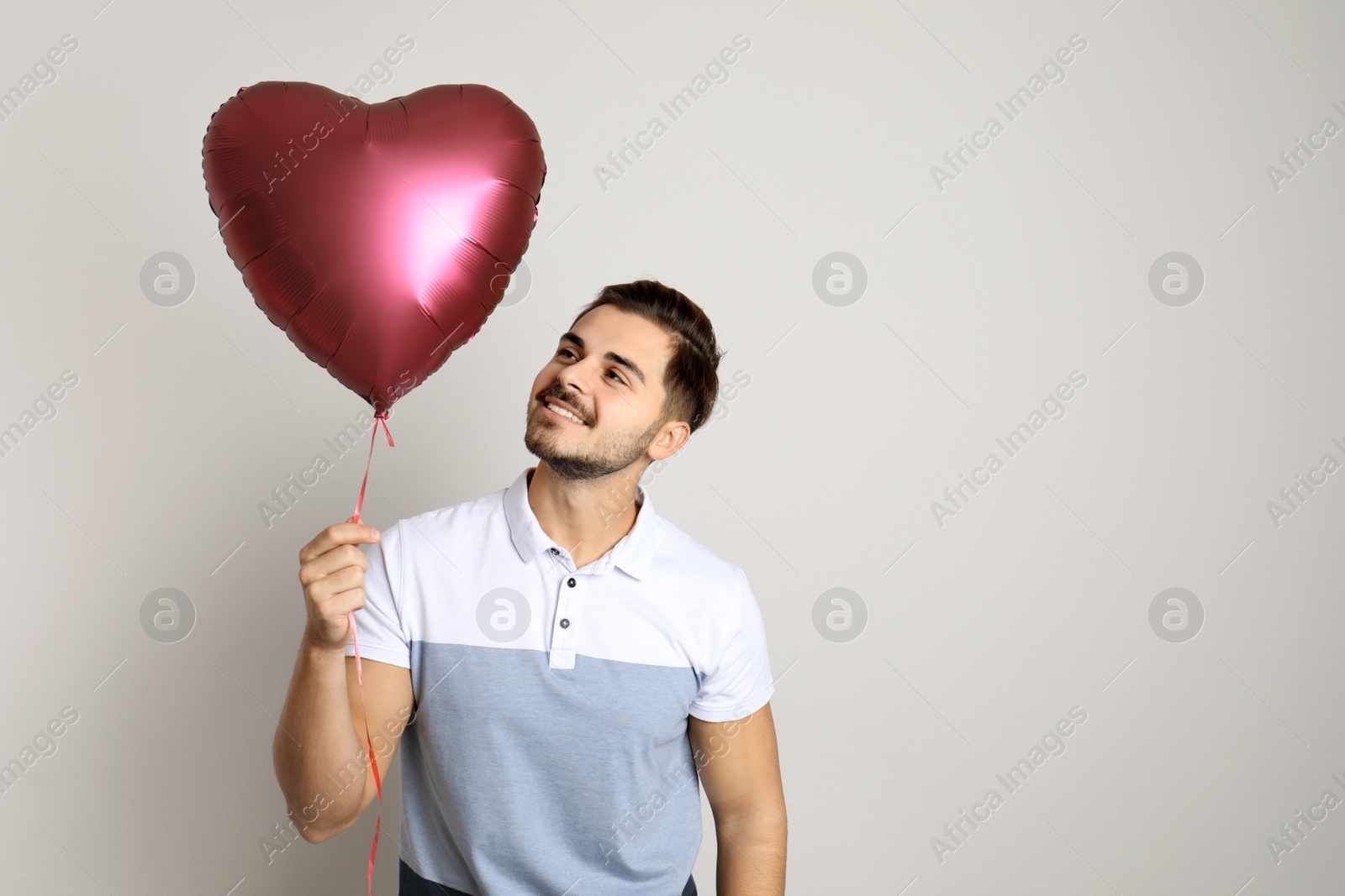 Photo of Portrait of young man with heart shaped balloon on light background. Space for text