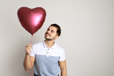 Portrait of young man with heart shaped balloon on light background. Space for text