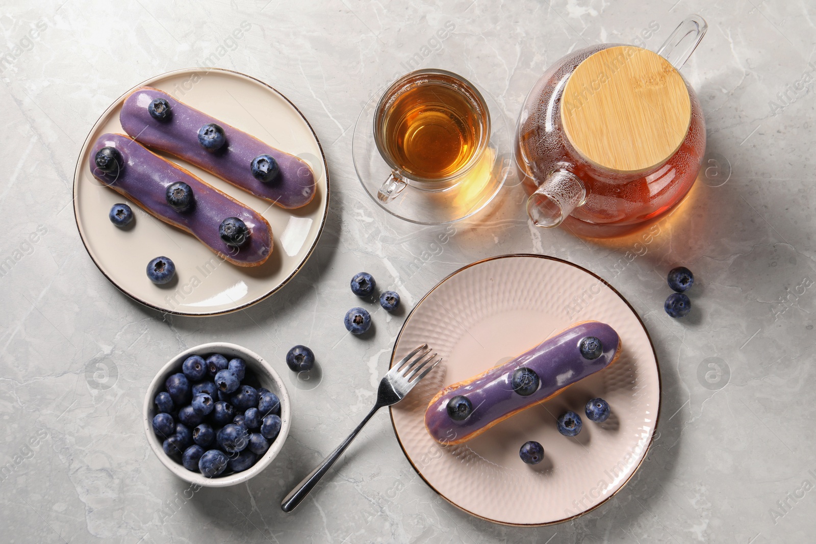 Photo of Tasty glazed eclairs with blueberries and tea on grey marble table, flat lay