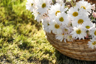 Photo of Beautiful wild flowers in wicker basket on green grass outdoors, closeup. Space for text