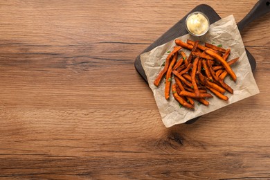 Photo of Board with delicious sweet potato fries and sauce on wooden table, top view. Space for text