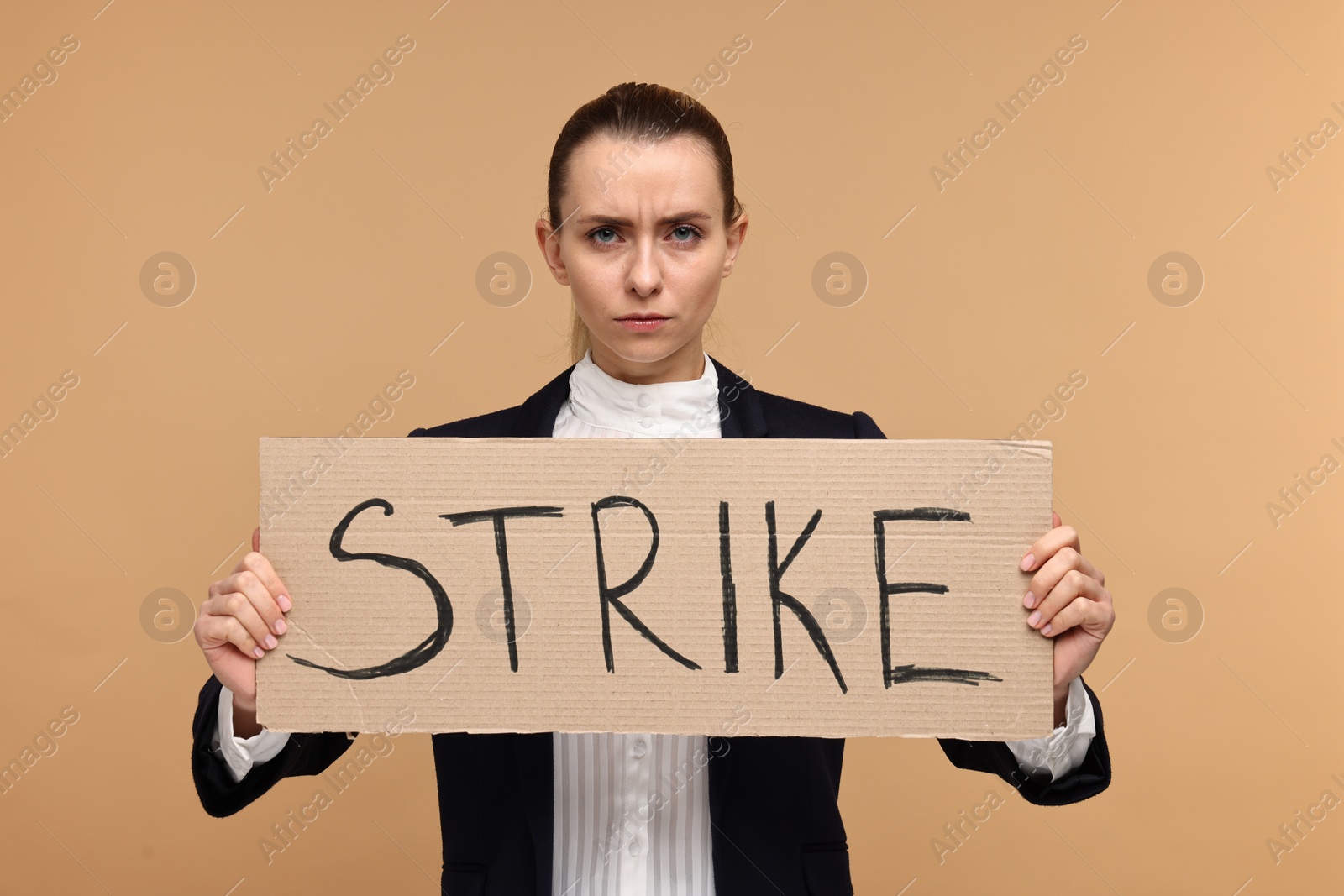 Photo of Angry woman holding cardboard banner with word Strike on beige background