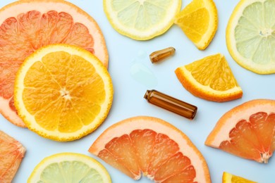 Broken skincare ampoule with vitamin C and slices of different citrus fruits on light blue background, flat lay