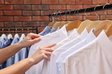 Photo of Dry-cleaning service. Woman taking shirt from rack against brick wall, closeup