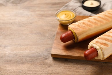 Photo of Tasty french hot dogs and dip sauces on wooden table, space for text