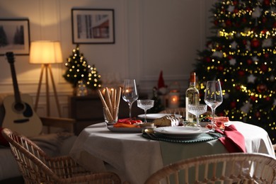Christmas table setting with bottle of wine, appetizers and dishware in room