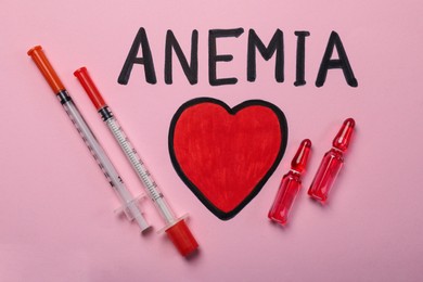 Photo of Word Anemia, syringes, ampoules and drawn heart on pink background, flat lay