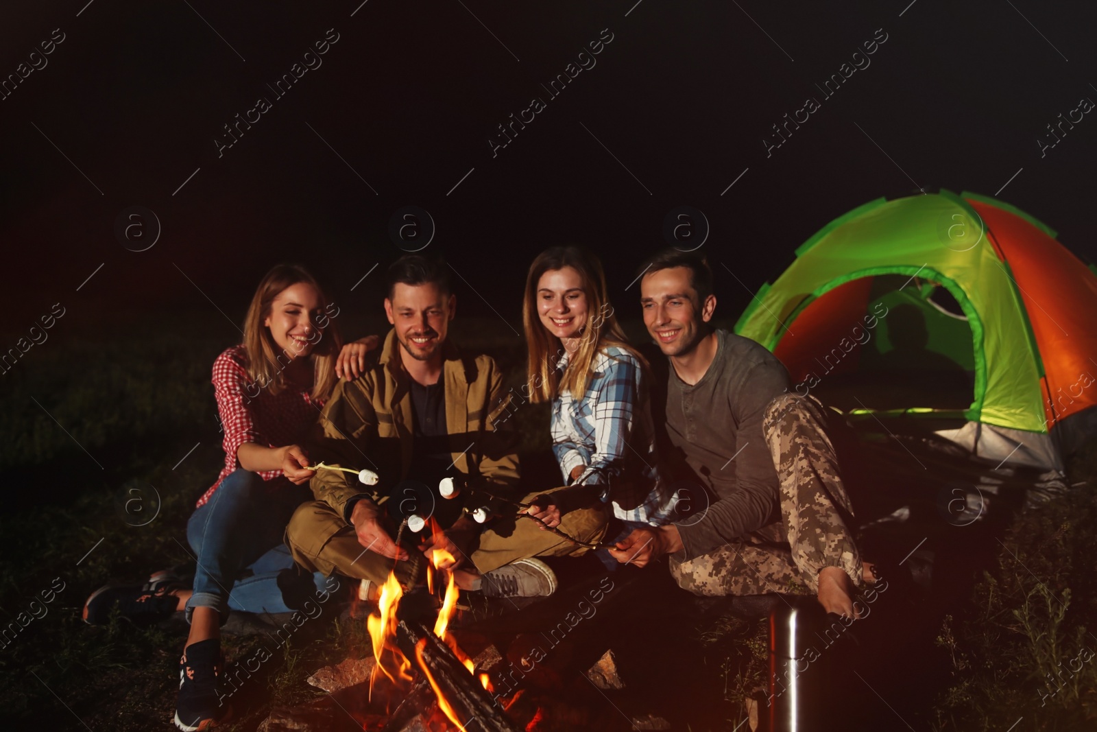 Photo of Friends frying marshmallows on bonfire at night. Camping season