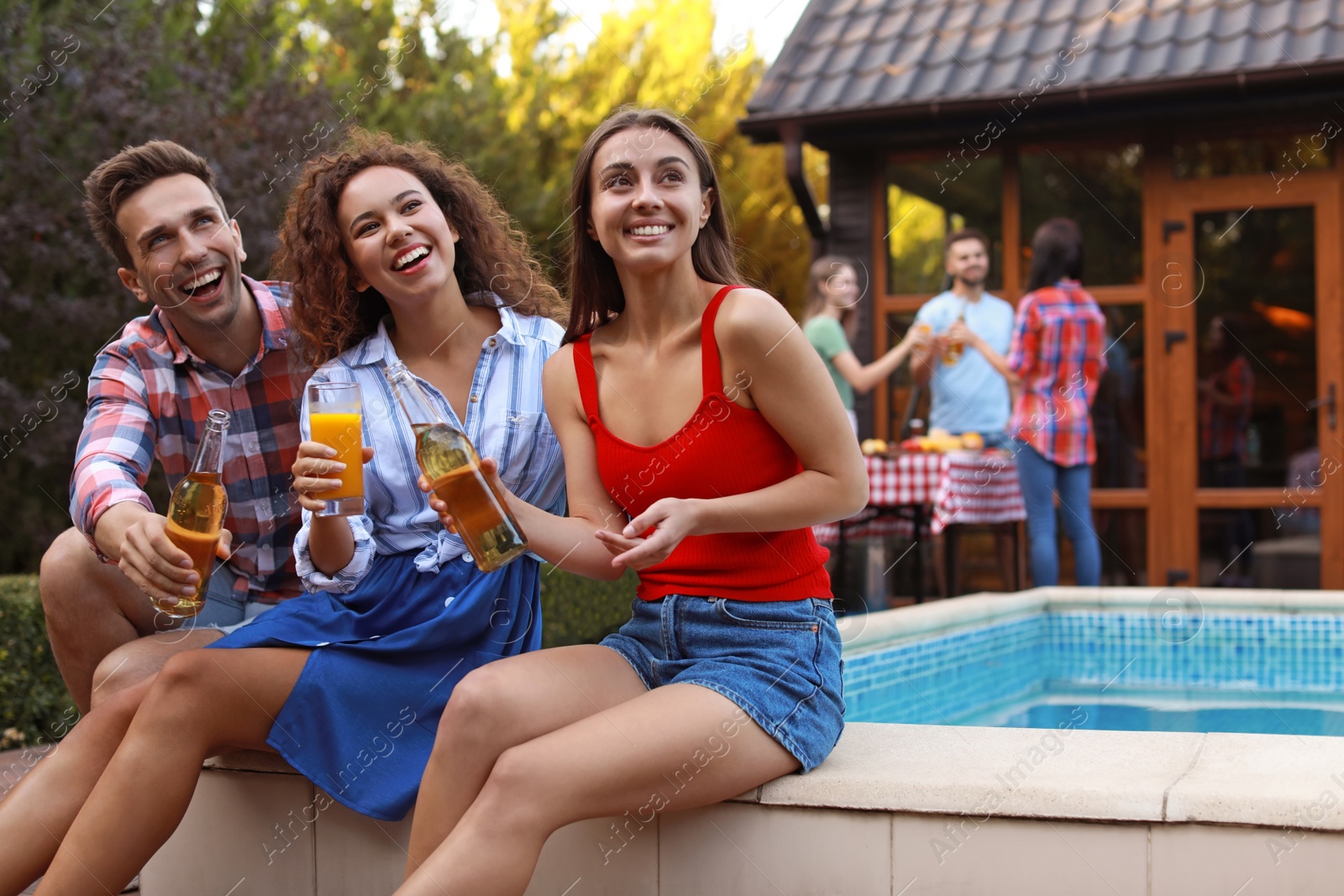 Photo of Happy friends with drinks at barbecue party near swimming pool outdoors