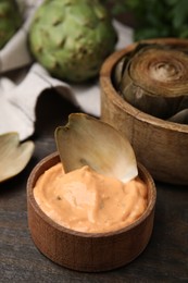Photo of Delicious cooked artichoke with tasty sauce on wooden table, closeup