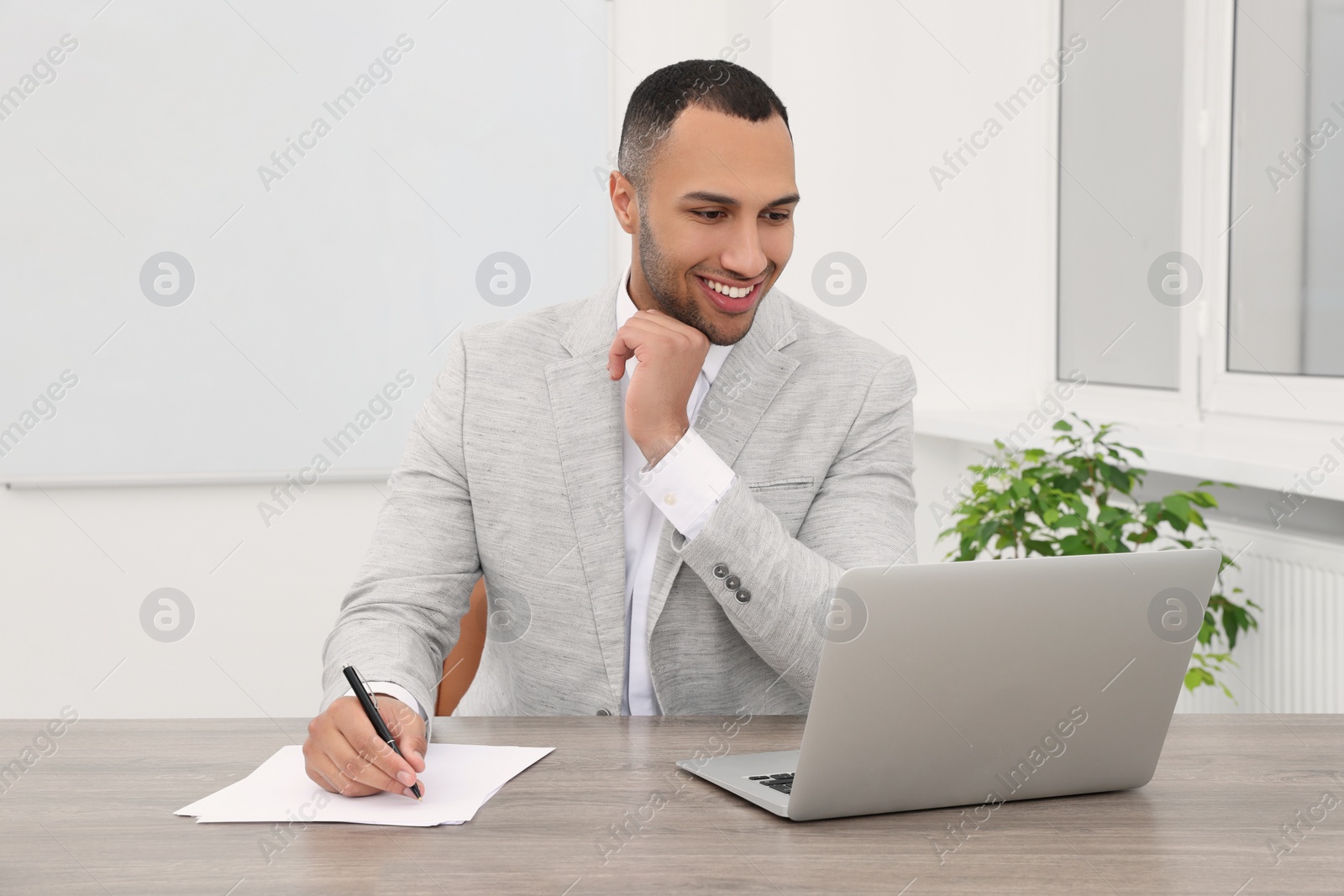 Photo of Happy young intern working with laptop at table in modern office