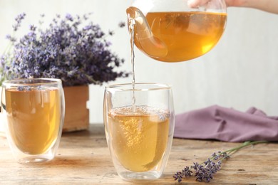 Photo of Woman pouring delicious lavender tea into glass at wooden table, closeup