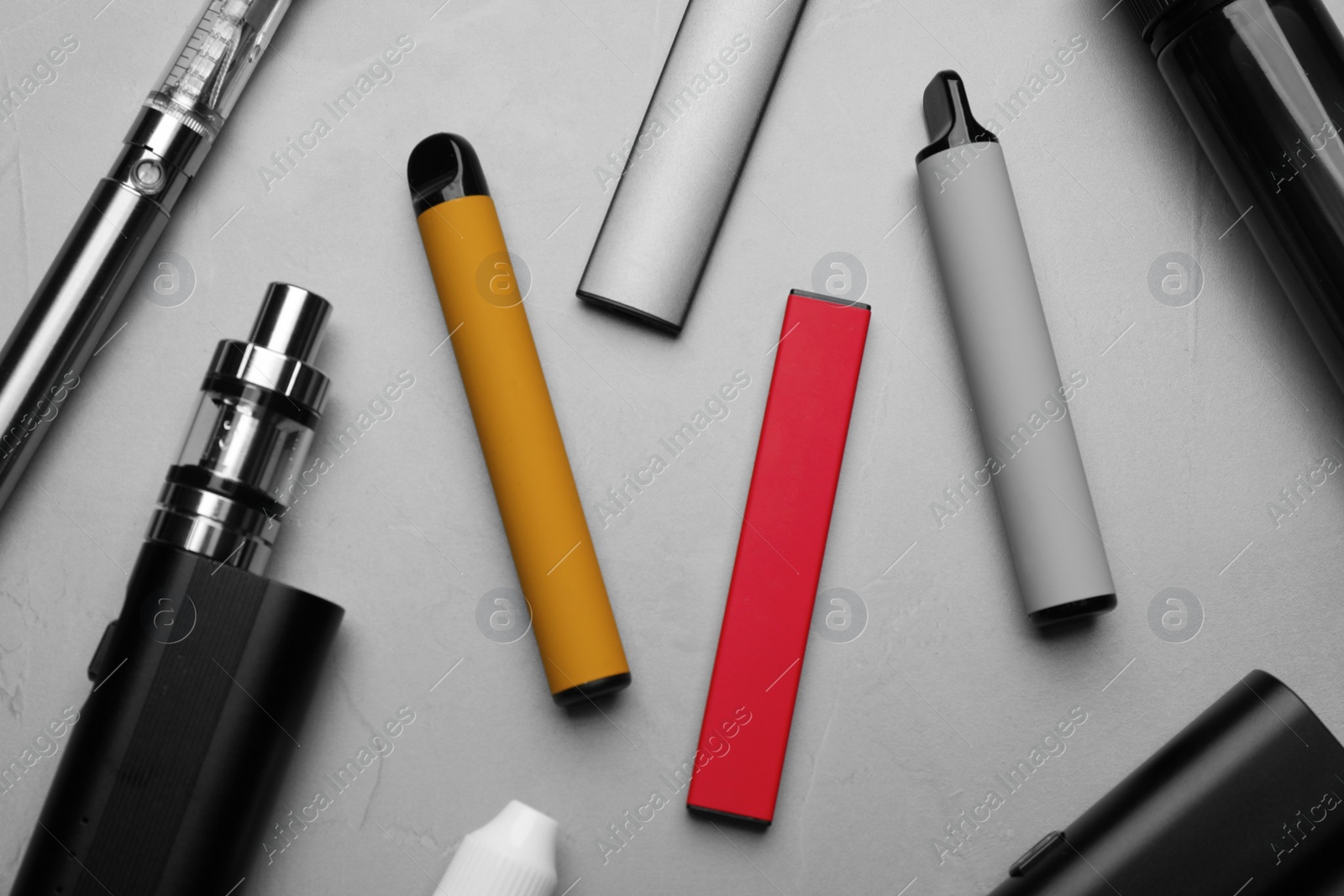 Photo of Different electronic cigarettes on grey table, flat lay. Smoking alternative