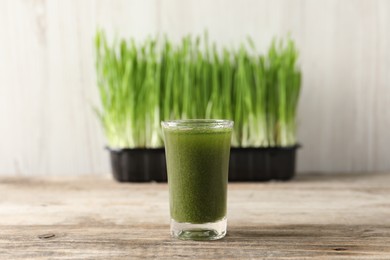 Photo of Wheat grass drink in shot glass on wooden table, closeup