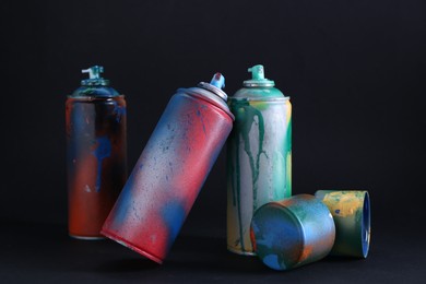 Photo of Many spray paint cans with caps on dark background
