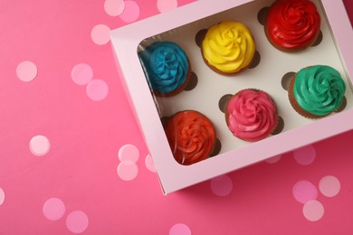 Box with different cupcakes and confetti on pink background, flat lay. Space for text