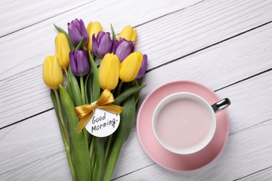 Photo of Cup of hot drink, beautiful tulips and card with text Good Morning on white wooden table, flat lay