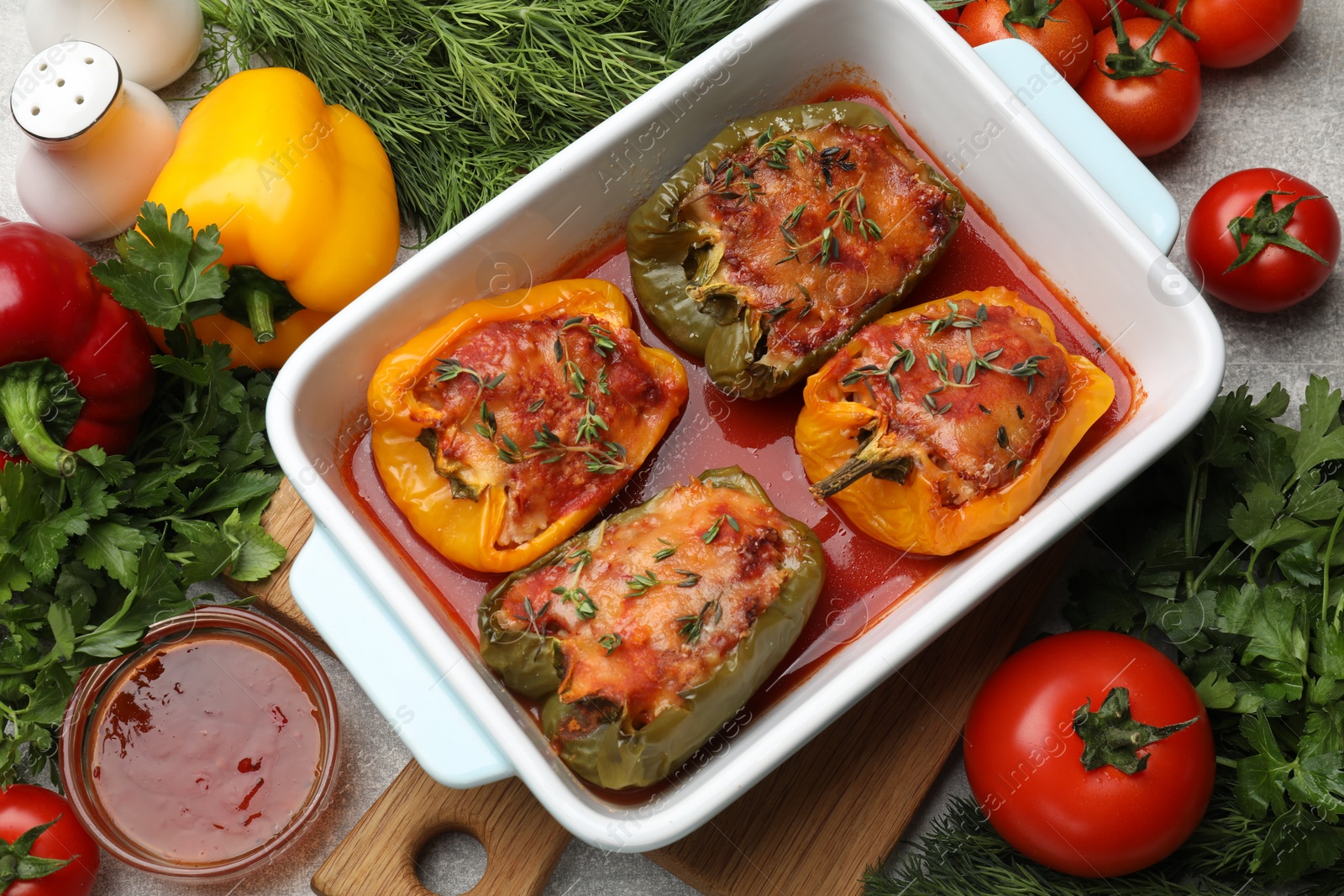 Photo of Tasty stuffed peppers in dish and ingredients on grey table, above view