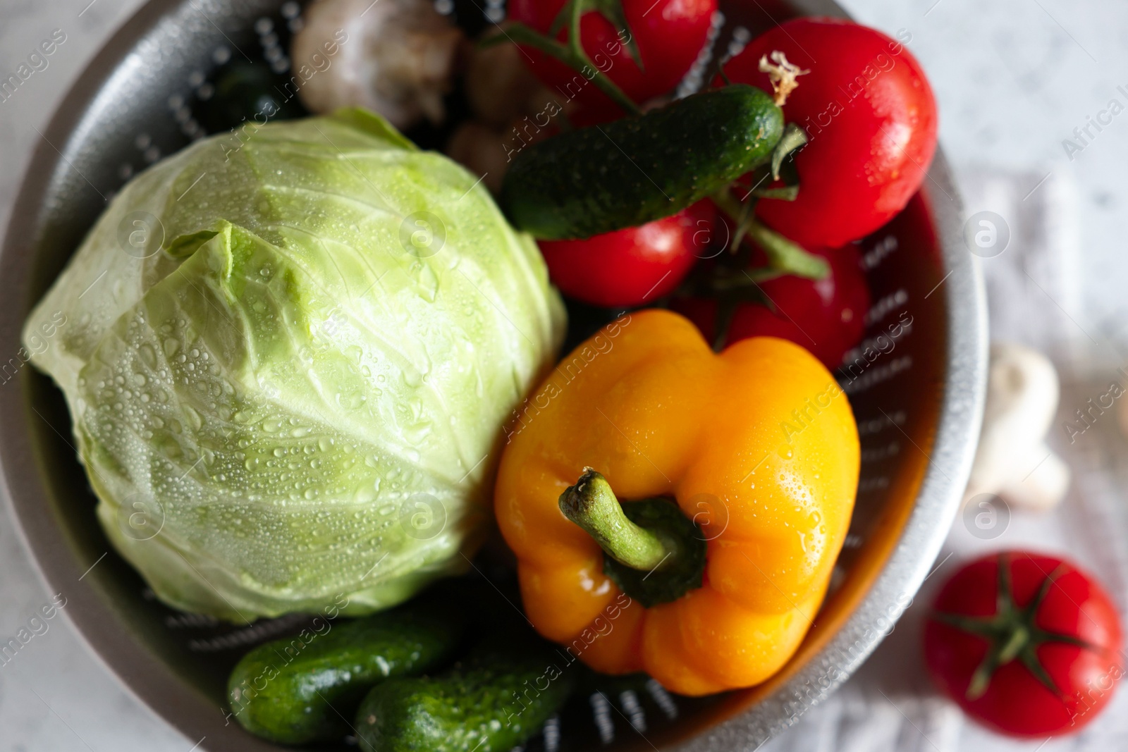 Photo of Metal colander with different wet vegetables on white textured table, top view