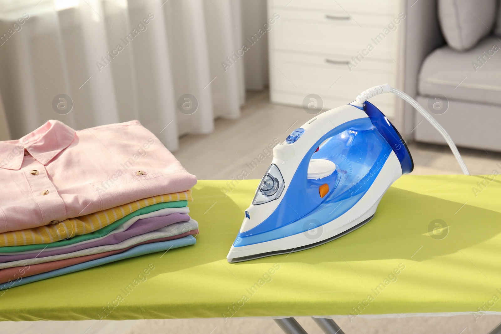 Photo of Board with modern iron and clean laundry at home