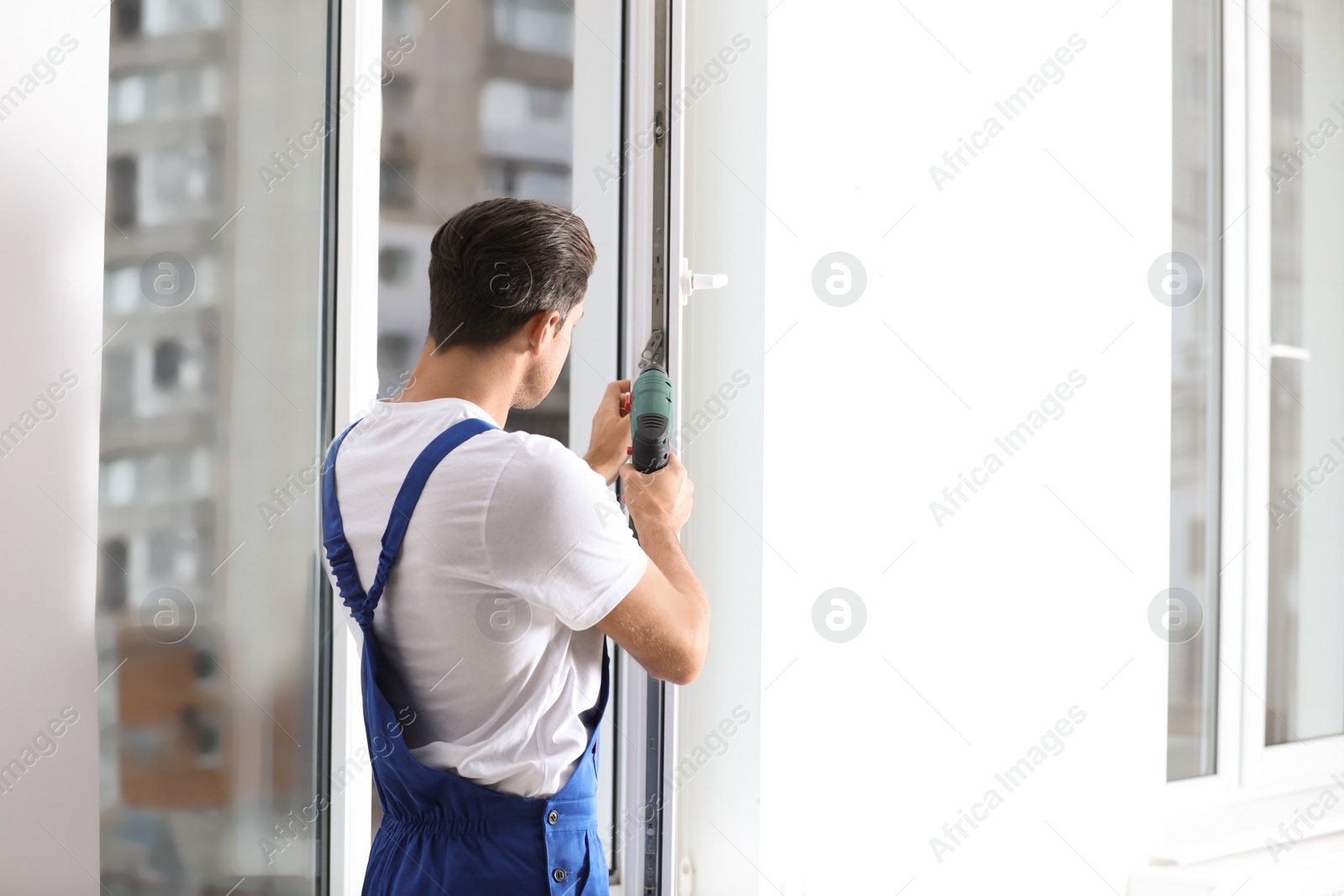 Photo of Construction worker repairing plastic window with screwdriver indoors