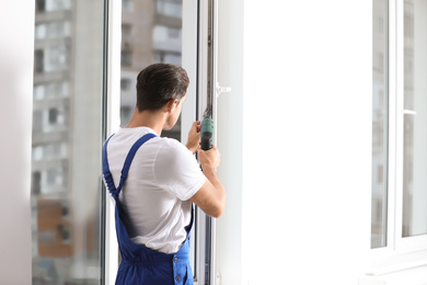 Construction worker repairing plastic window with screwdriver indoors