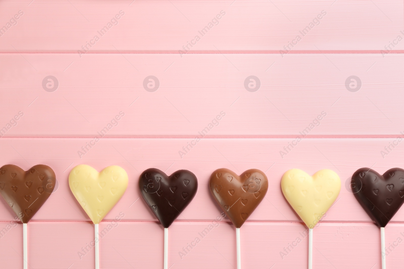 Photo of Different chocolate heart shaped lollipops on pink wooden table, flat lay. Space for text