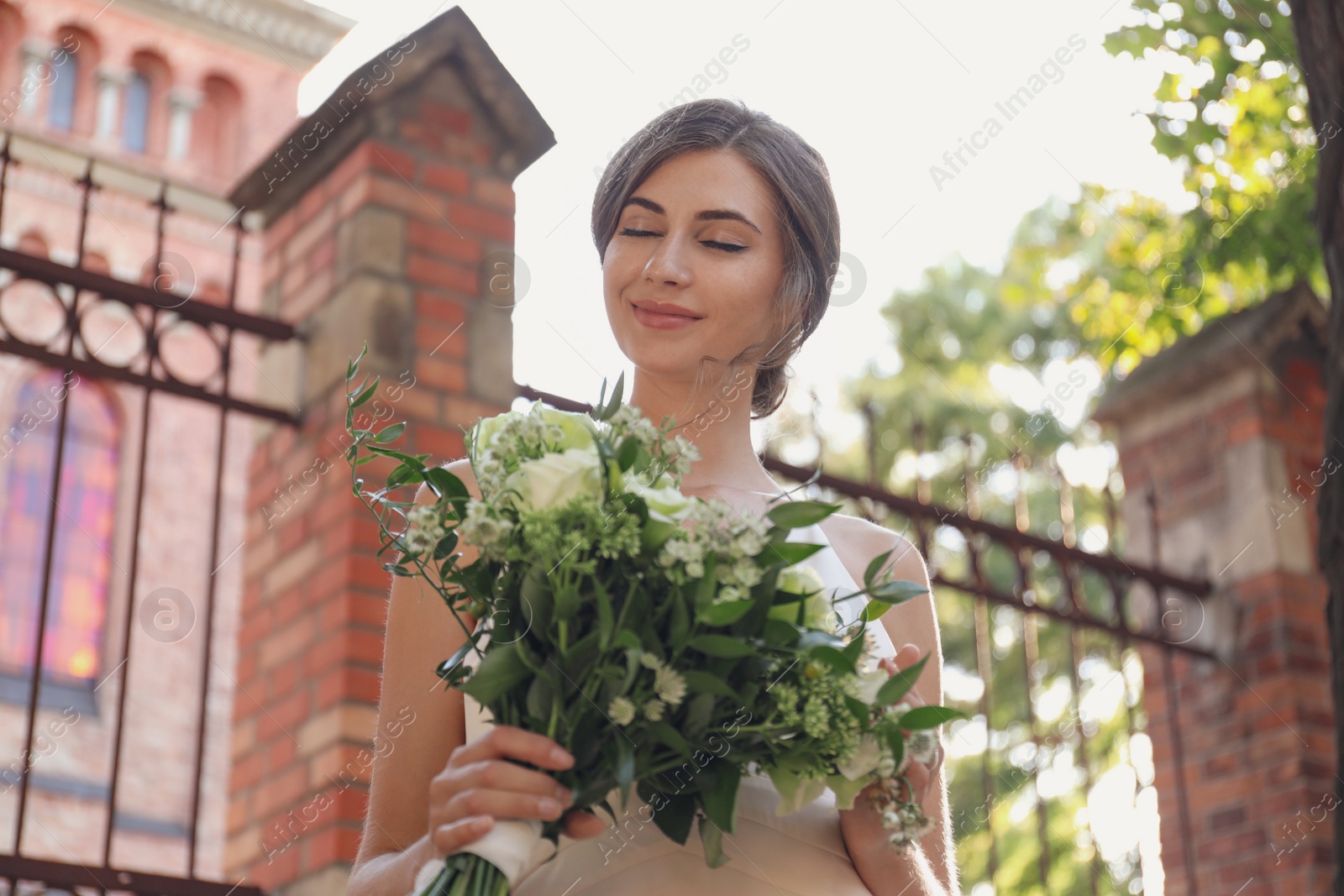 Photo of Gorgeous bride in beautiful wedding dress with bouquet near church