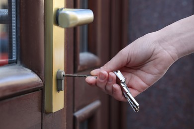 Photo of Woman opening door with key outdoors, closeup