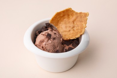 Photo of Tasty chocolate ice cream and piece of waffle cone in bowl on beige background, closeup