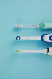 Photo of Electric toothbrushes on light blue background, flat lay