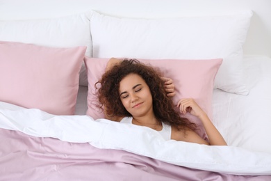 Photo of Young African-American woman sleeping on soft pillow, top view. Bedtime