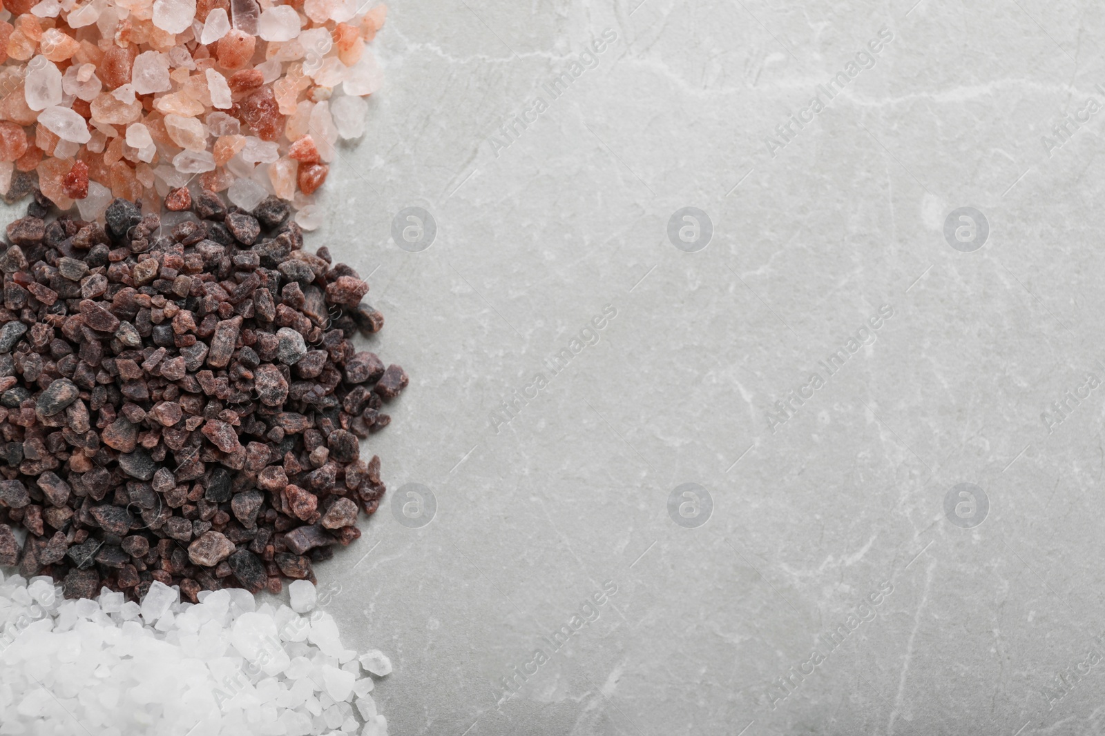 Photo of Different kinds of salt on light grey marble table, flat lay. Space for text