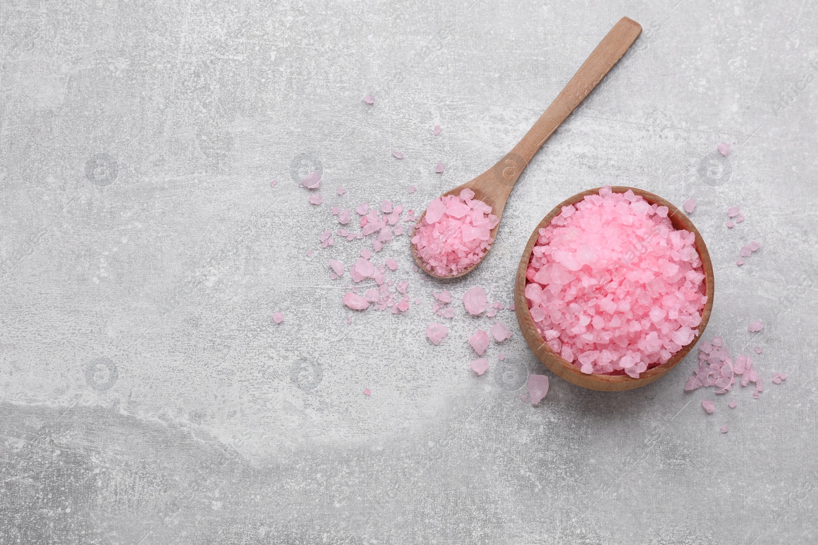 Photo of Bowl and spoon with pink sea salt on light grey table, flat lay. Space for text