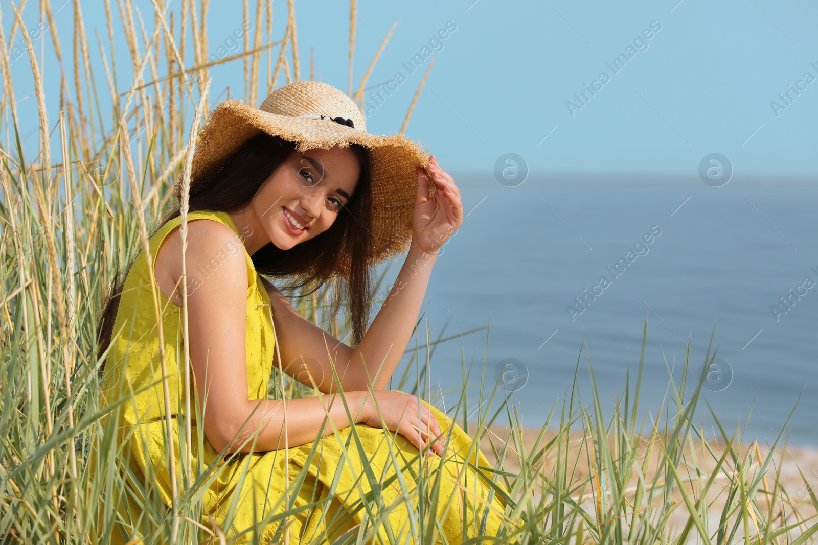 Photo of Beautiful young woman wearing straw hat on beach. Stylish headdress