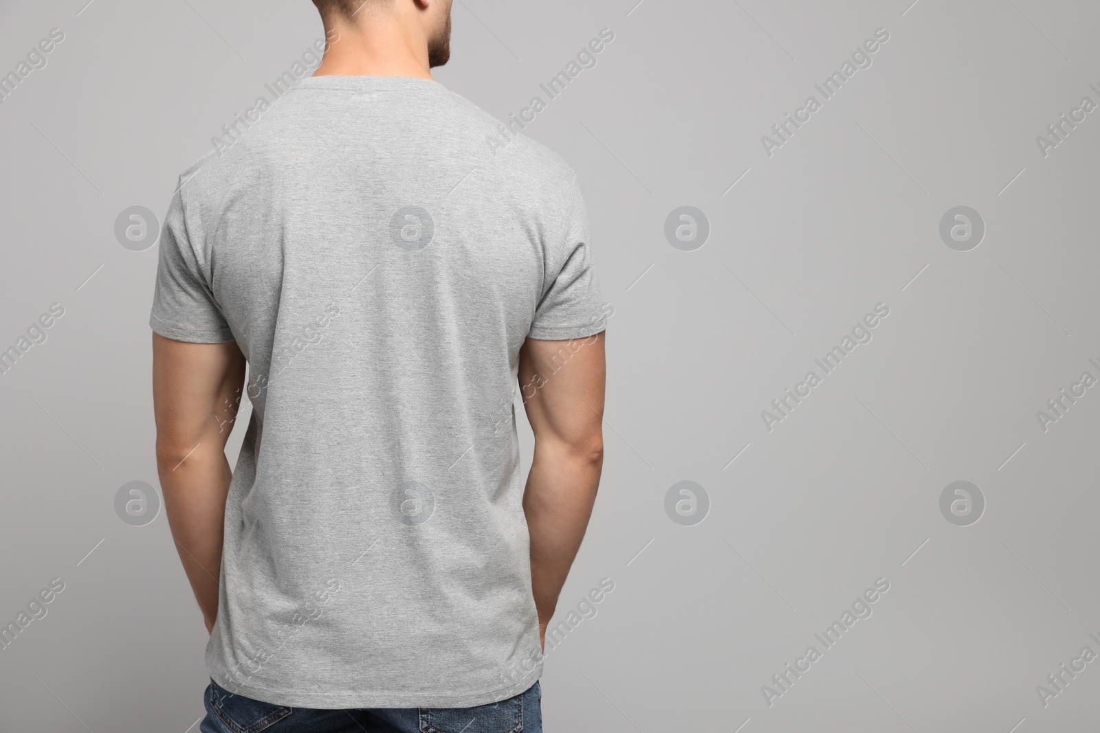 Photo of Man wearing blank t-shirt on light grey background, back view. Mockup for design